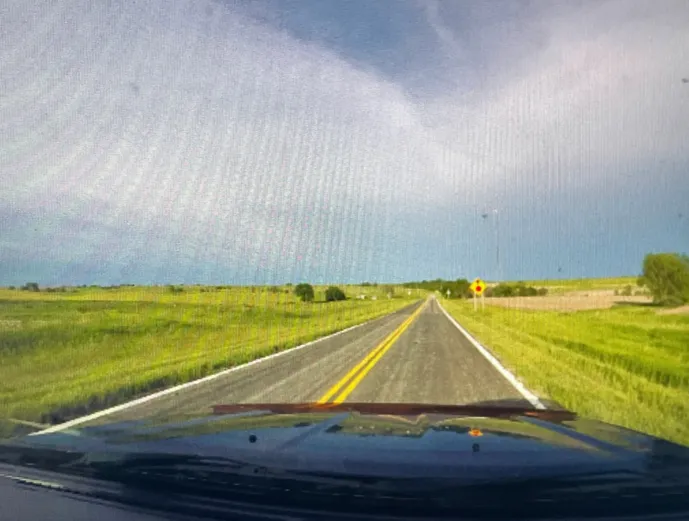 A screnshot of AmericaOS: What appears to be a view from the inside of a car's driver seat, looking out at a field of grass.