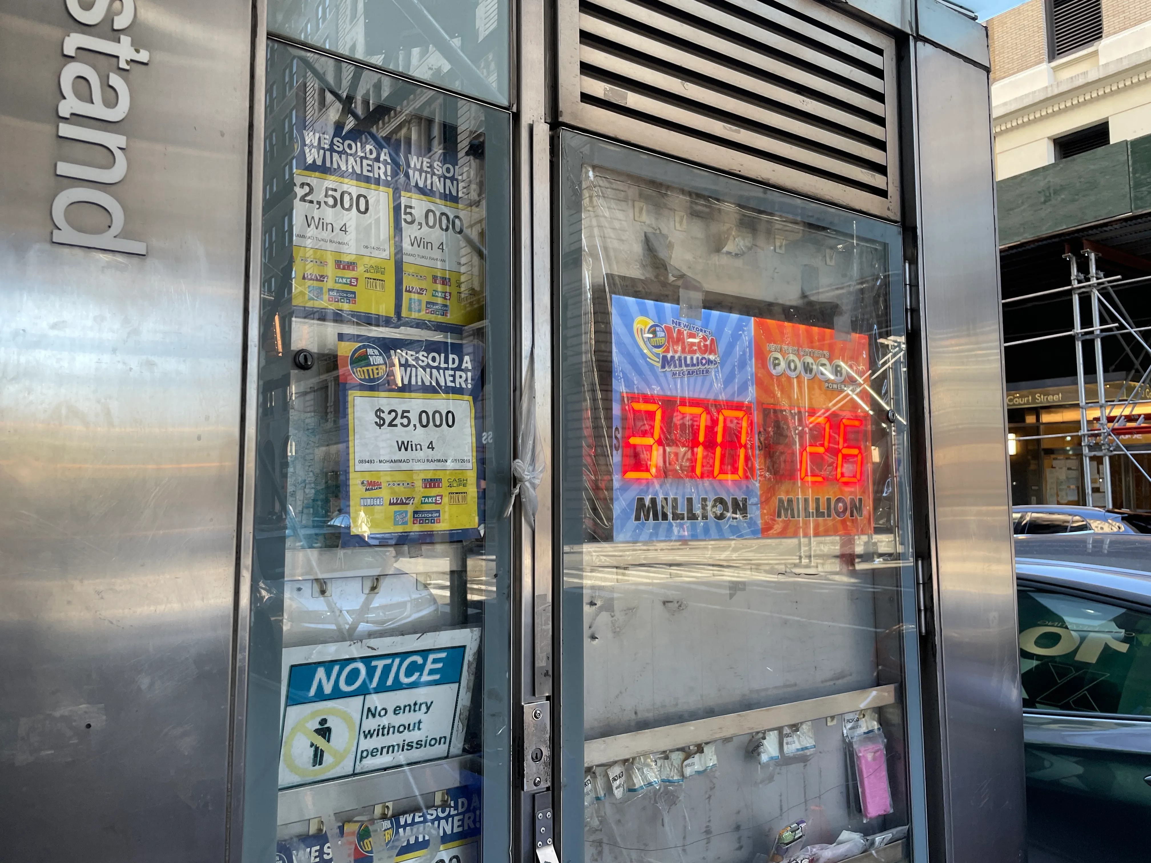 A photograph of a newspaper stand and lottery LED sign somewhere in downtown Brooklyn.