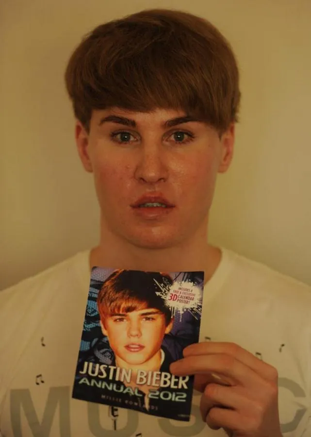 A photograph of a Justin Beiber lookalike. The lookalike is holding an event flyer for a Justin Beiber concert.